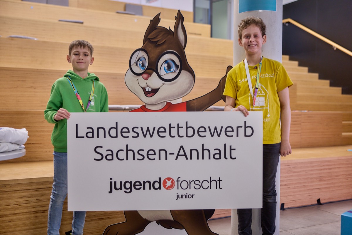 Zwei junge Teilnehmende vor dem Schild Landeswettbewerb Sachsen-Anhalt